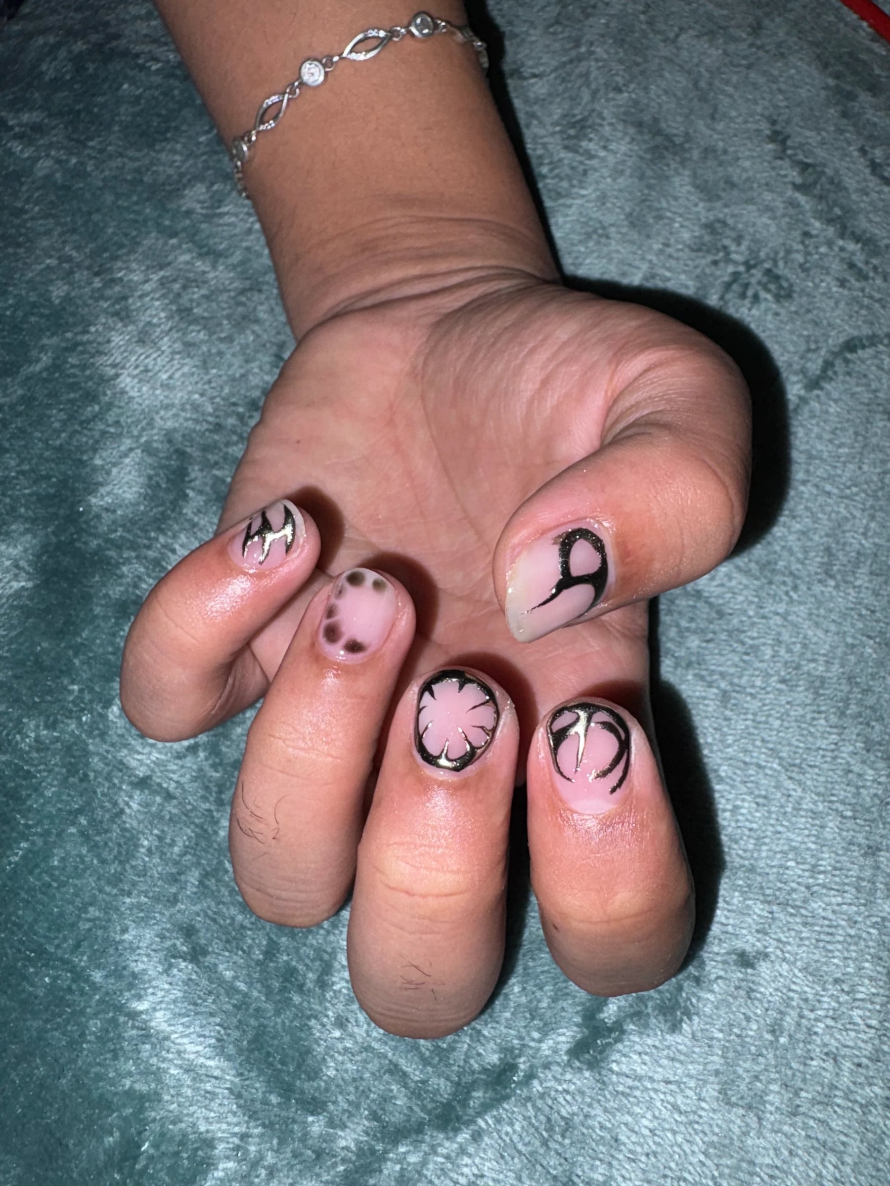Close-up of Kyro’s pink nail art with black abstract curves and metallic silver details against teal fabric